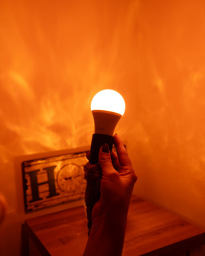 En hånd holder en tændt lampe op mod en væg i varmt skær