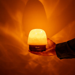 Den genopladelige natlampe Havie holdes i en hånd og spreder et varmt orange skær.