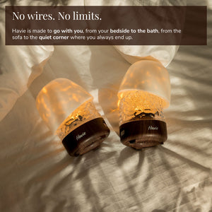 Two cordless, rechargeable Havie lamps glowing warmly on a bed.