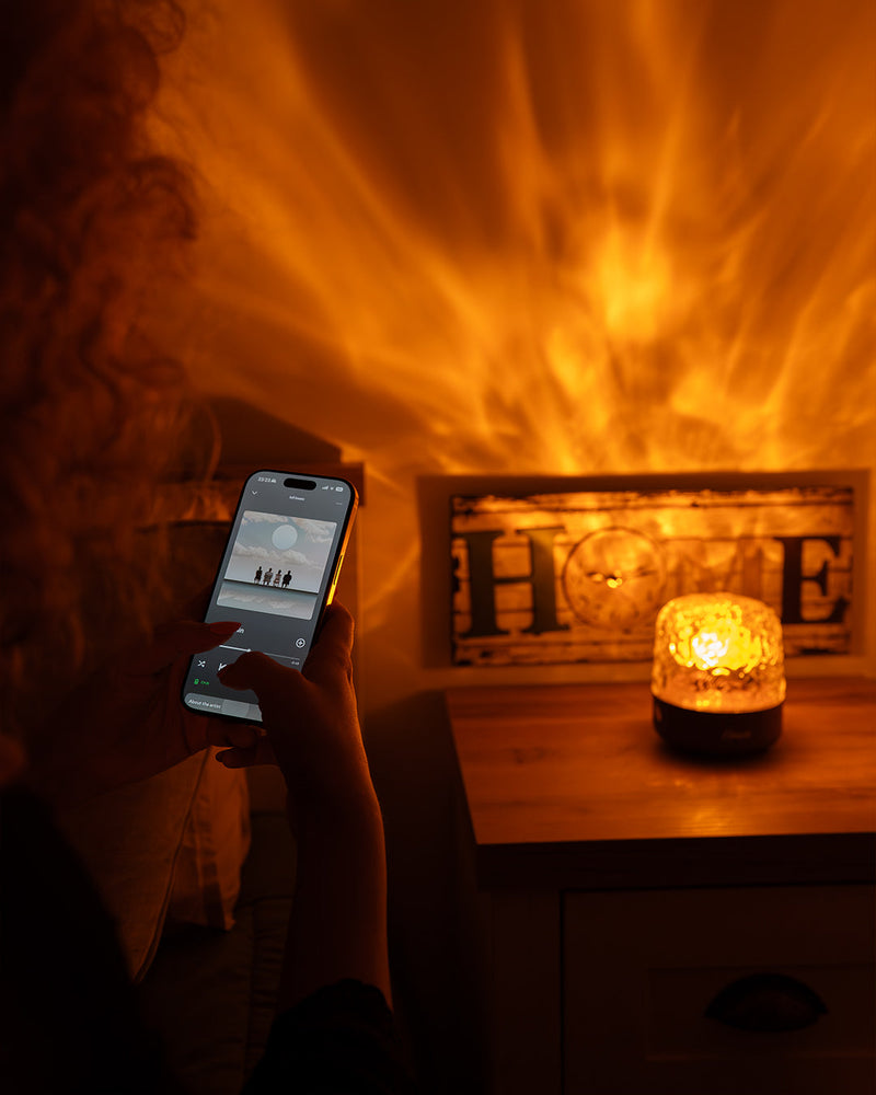 En hånd vælger lyd på mobilen, mens Havie lyser på natbordet, og flammeskæret fylder væggen